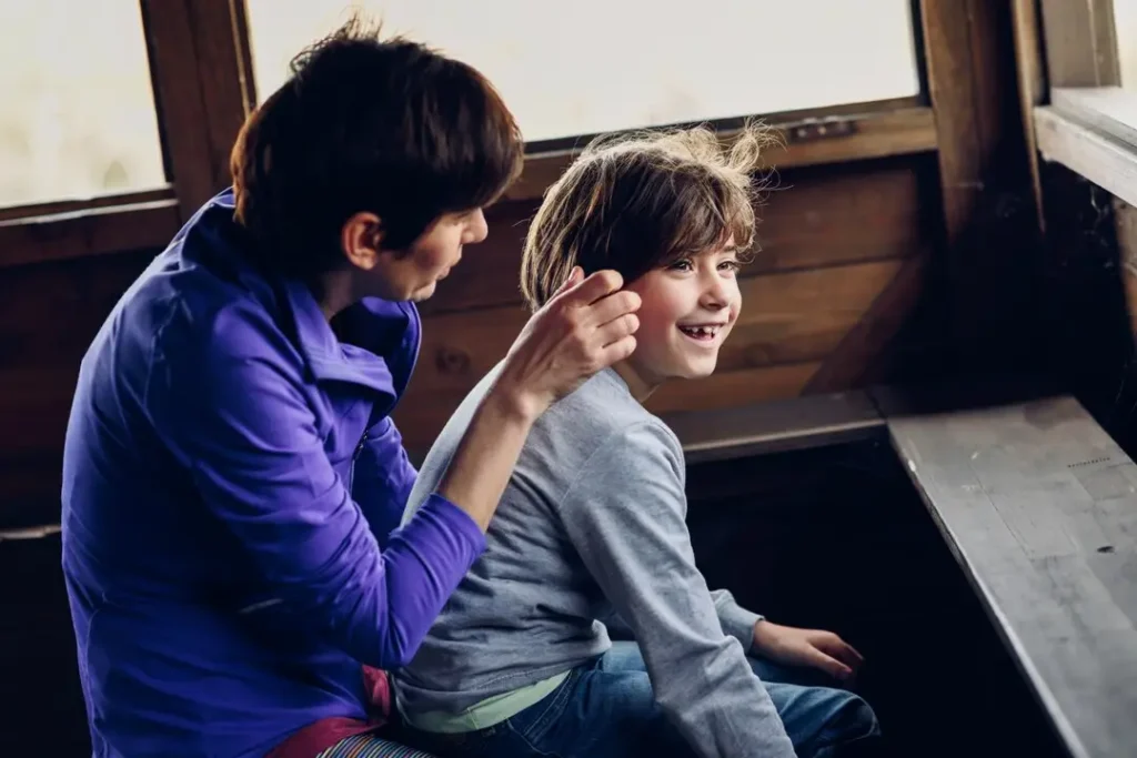 Parent gently adjusting a child’s hair while they sit together indoors, reflecting attentive care and everyday parenting support.