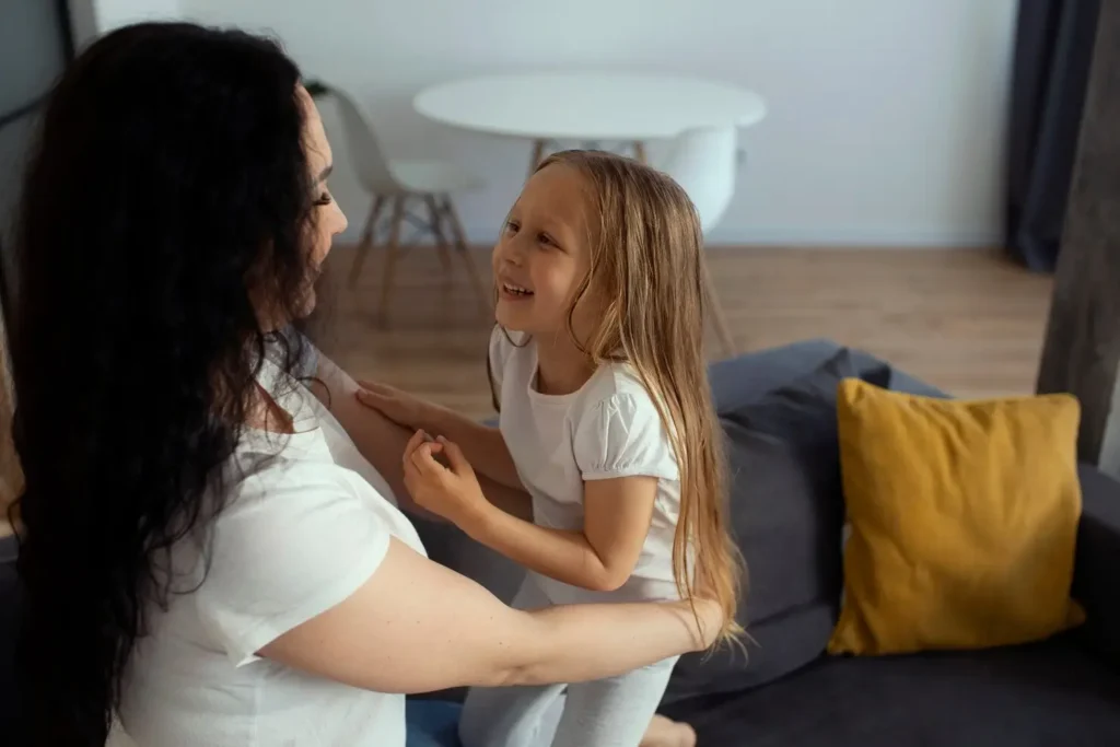 Parent and child smiling at each other while sitting together on a couch, reflecting warmth, connection, and supportive parenting.