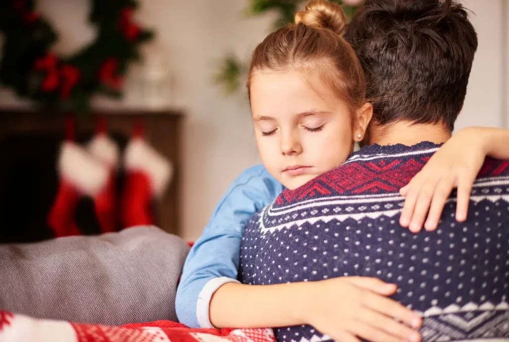 Child resting with eyes closed while hugging a parent, conveying comfort, security, and emotional reassurance.