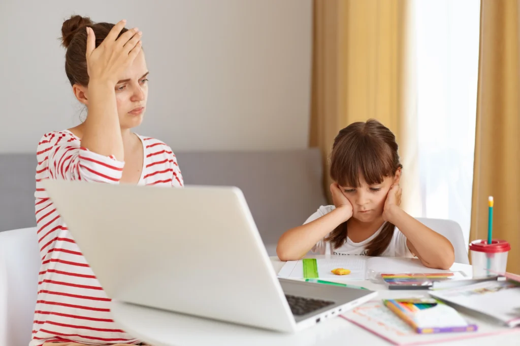 Mother and daughter sitting at table with laptop and schoolwork